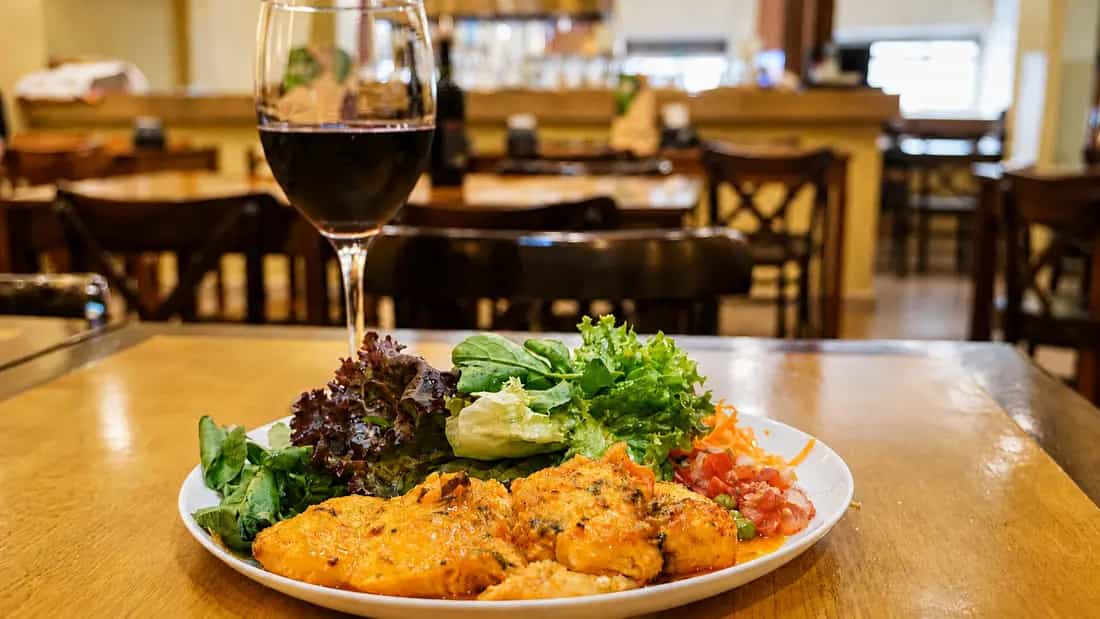 Prato montado com filés ao molho, folhas verdes, cenoura ralada e salada de tomate, sobre a mesa do salão